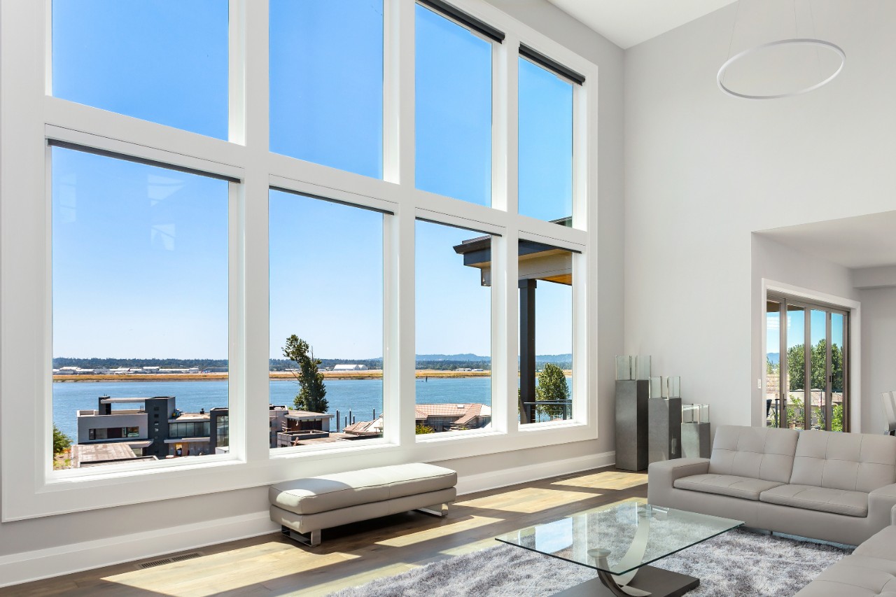 Beautiful modern living room in new luxury home with floor to ceiling fireplace surround and wall of windows with exterior view. Dining room can be seen as well.